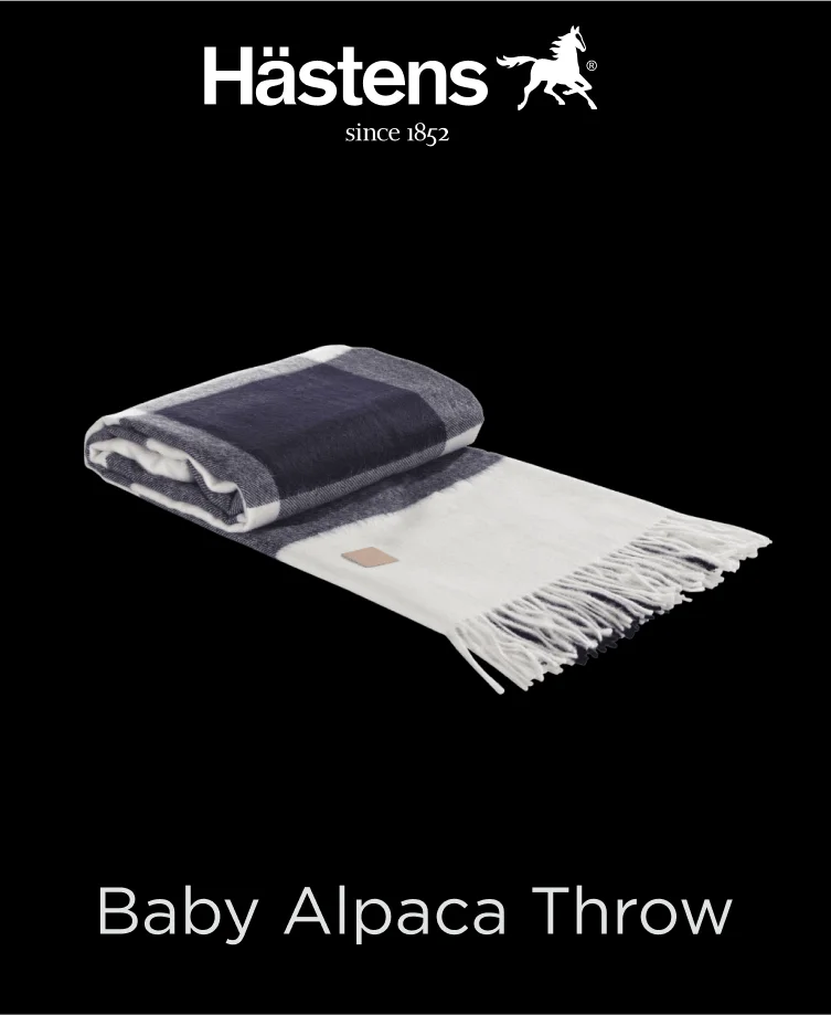 Luxurious Hastens Baby Alpaca Throw in a soft beige color, draped over a sofa